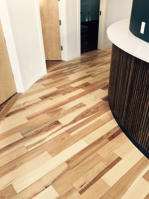 Wide-plank hickory flooring meeting a curved wood slat feature wall