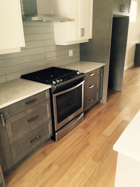 Kitchen with white oak flooring, grey cabinets and stainless range